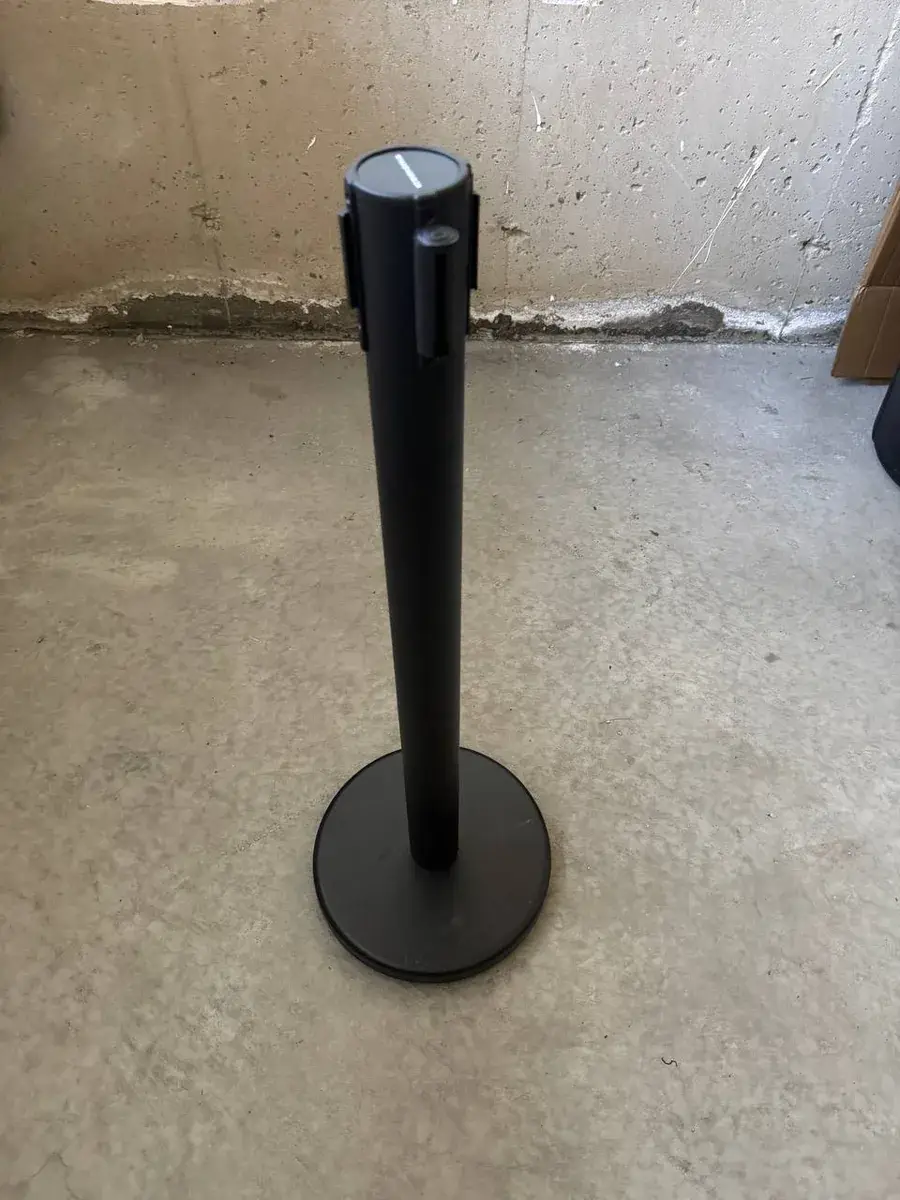 A single black belt stanchion photographed close up, the post and its round weighted base standing on a bare concrete floor.