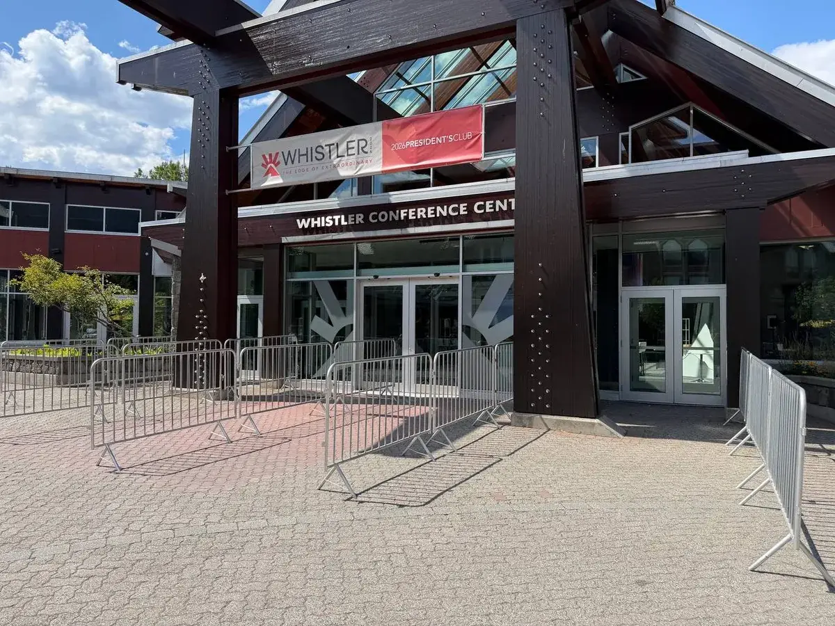 A run of galvanized steel barricades set out across the paved entrance of the Whistler Conference Centre, under the timber canopy over the doors.