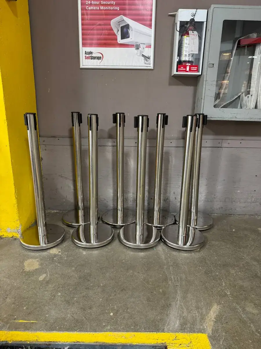 Chrome retractable belt stanchions standing in a row against a wall, stacked ready between events.