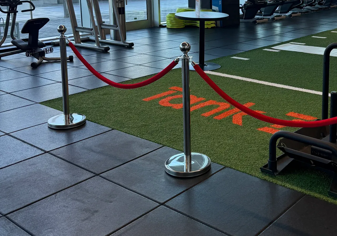 Two chrome rope posts carrying a red velvet rope across the floor of a fitness club