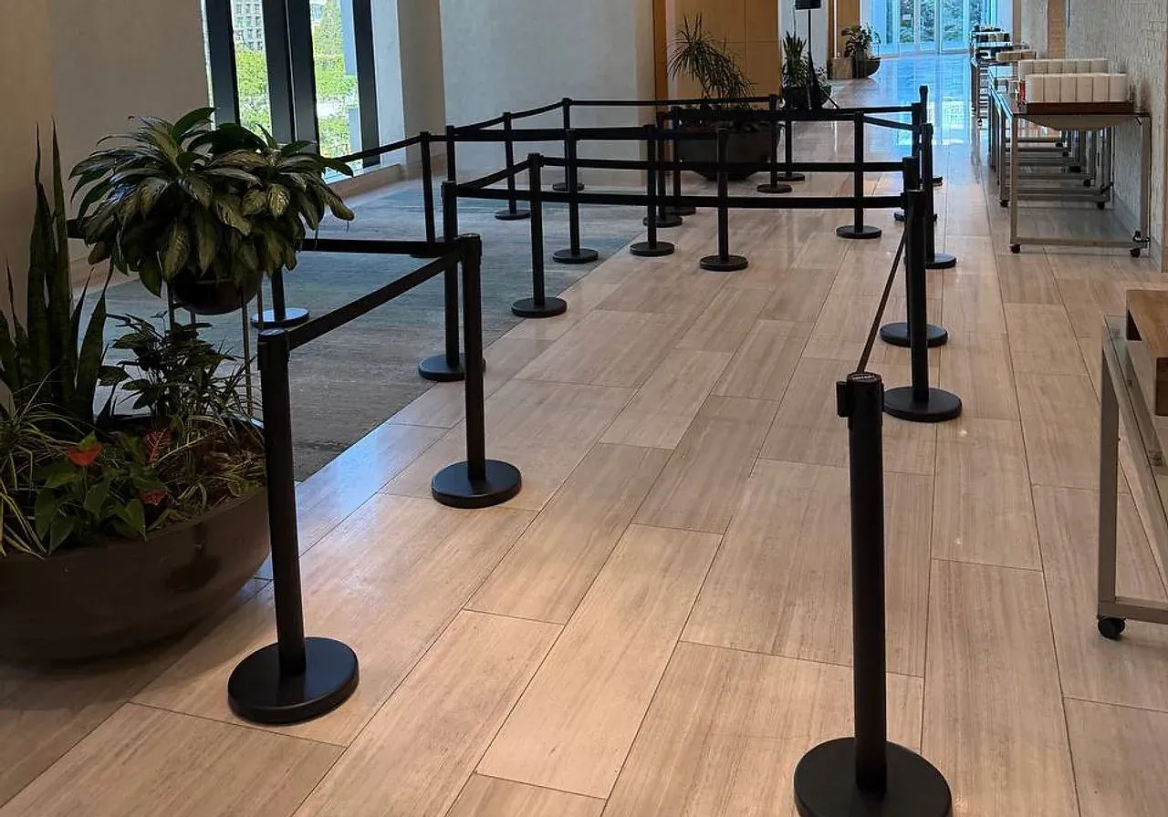 Black belt stanchions set as a switchback queue across the wooden floor of a building lobby