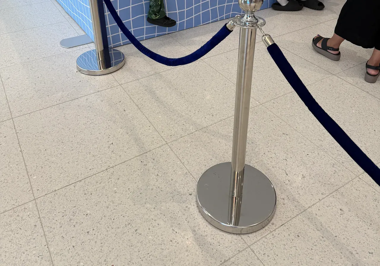 Chrome rope posts carrying a navy rope across a tiled concourse at a brand activation