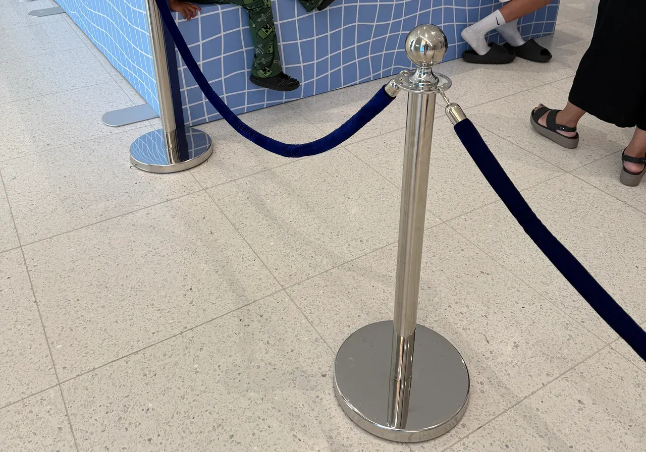 Chrome rope posts carrying a navy rope across a tiled concourse at a brand activation