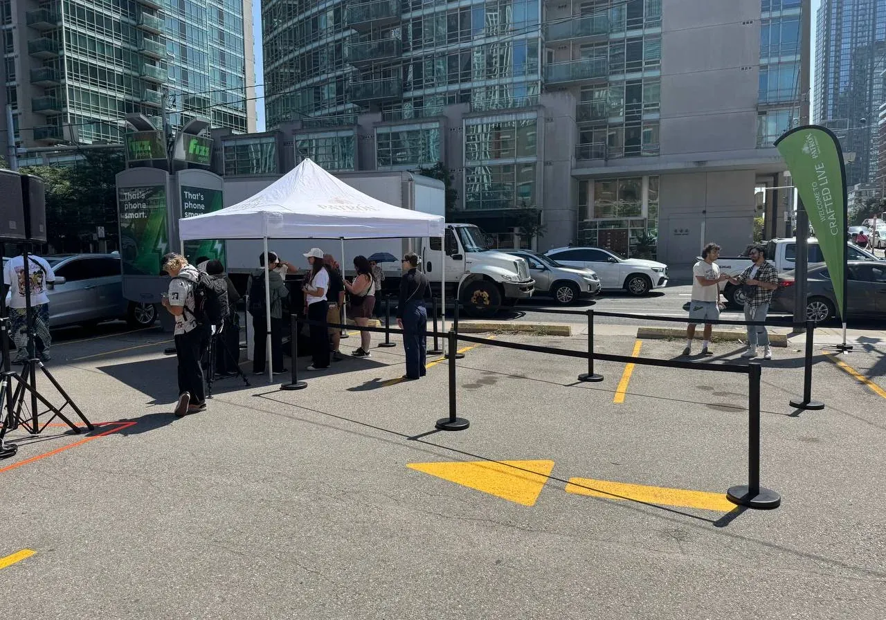 Black retractable belt stanchions run out as a queue line on a closed street, with a marquee and high-rise towers behind