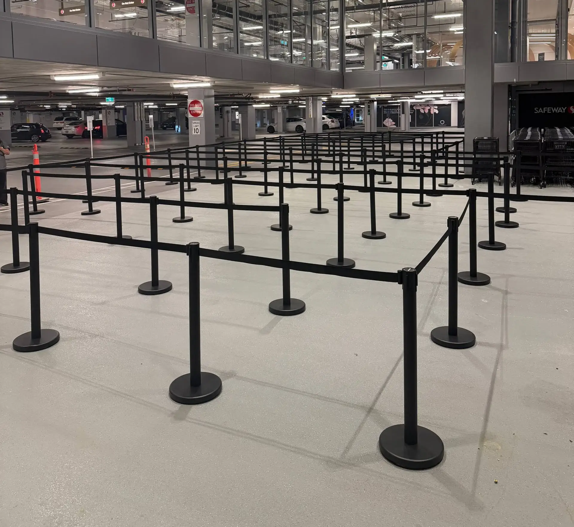 An empty switchback queue of black retractable-belt stanchions set out across a pale indoor floor