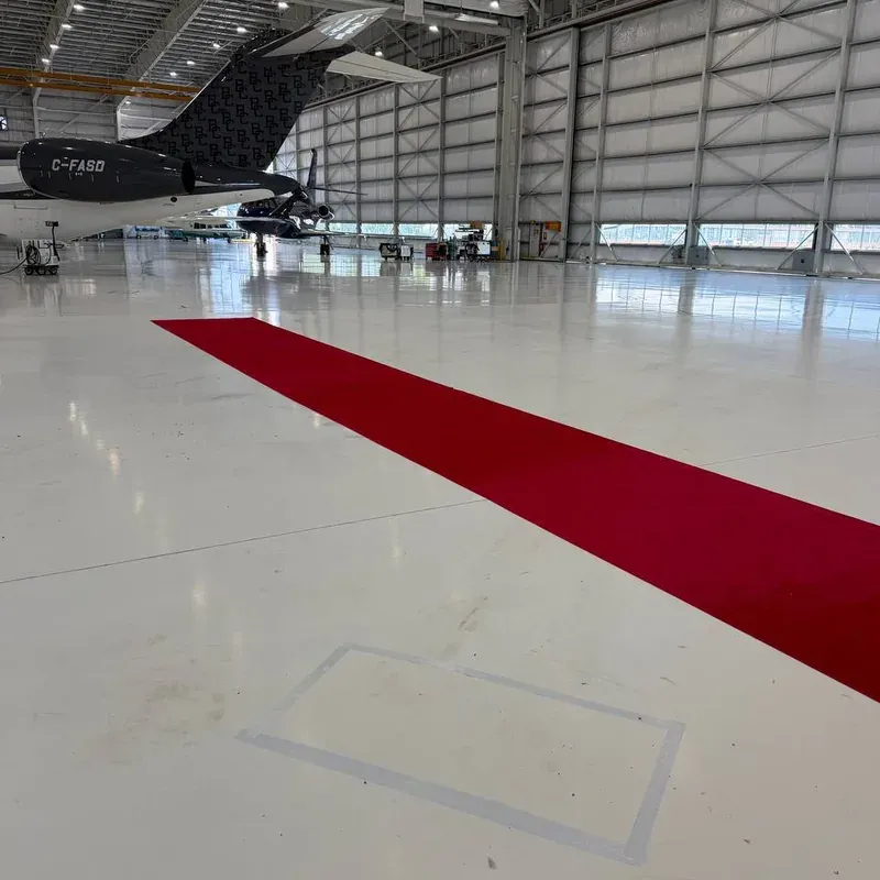 Red carpet runner laid the length of an aircraft hangar floor, with a jet parked at the far end.